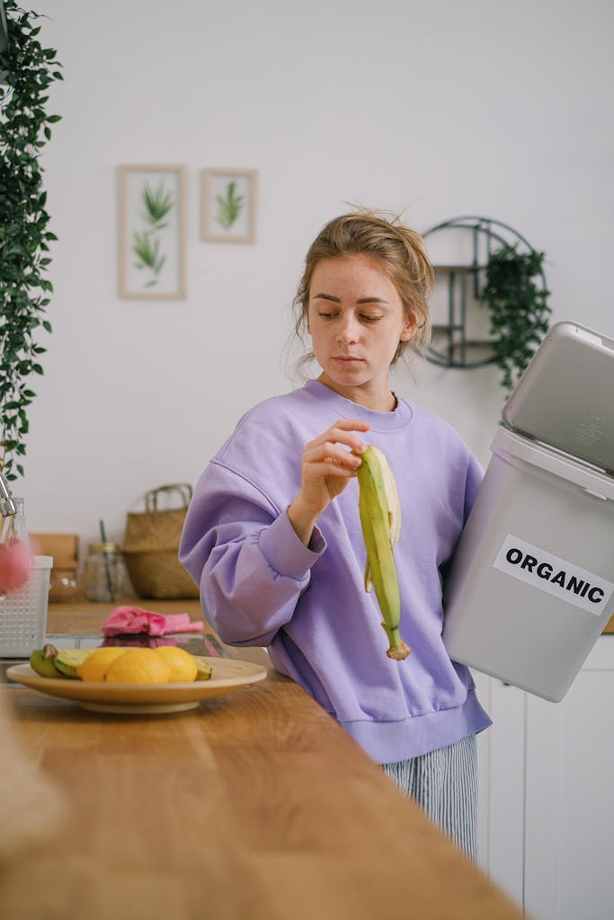 Monstera Deliciosa - Banana Compost Woman disposing banana peel into an organic waste bin in a cozy kitchen.